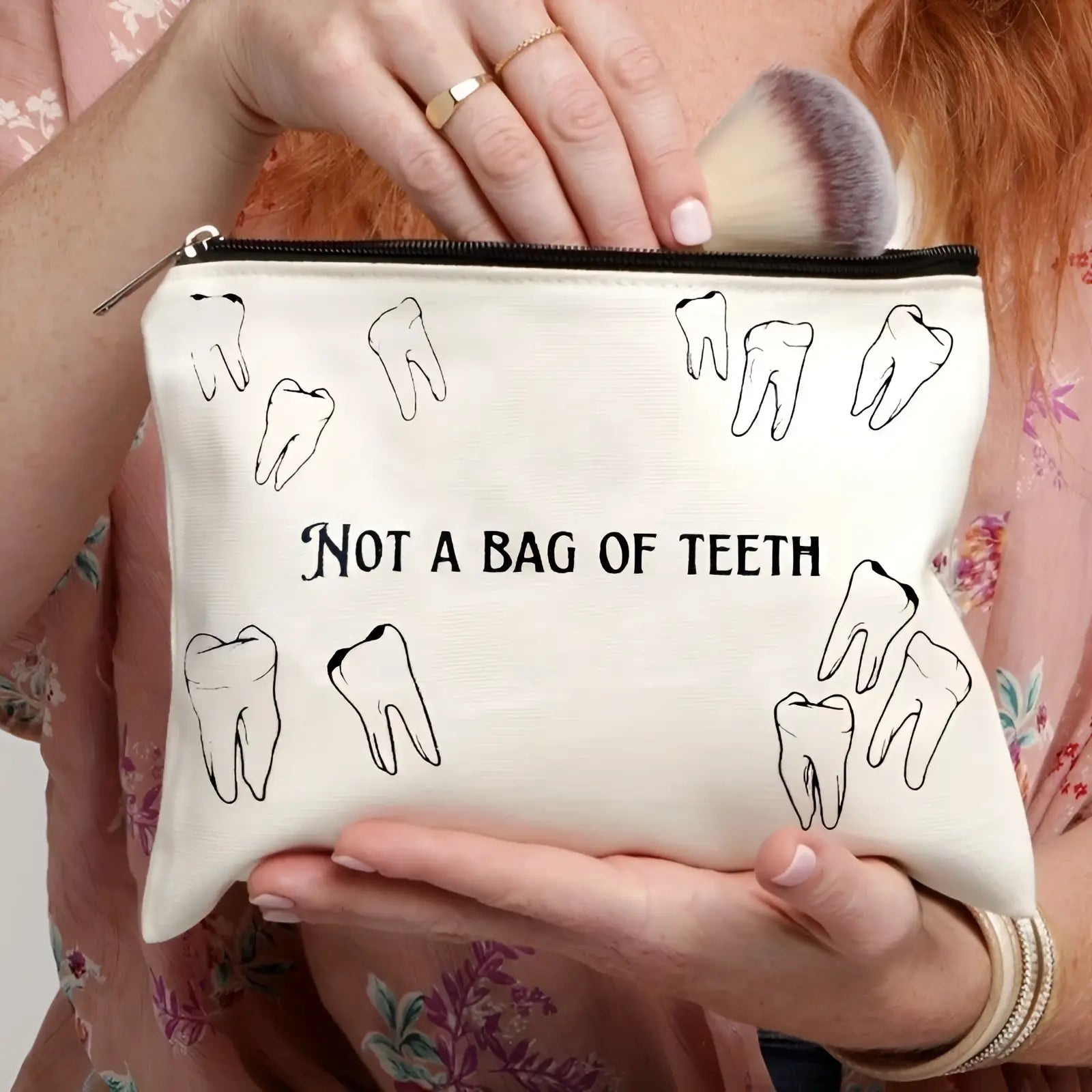Off-white canvas makeup bag with black tooth illustrations and not a bag of teeth text for travel use