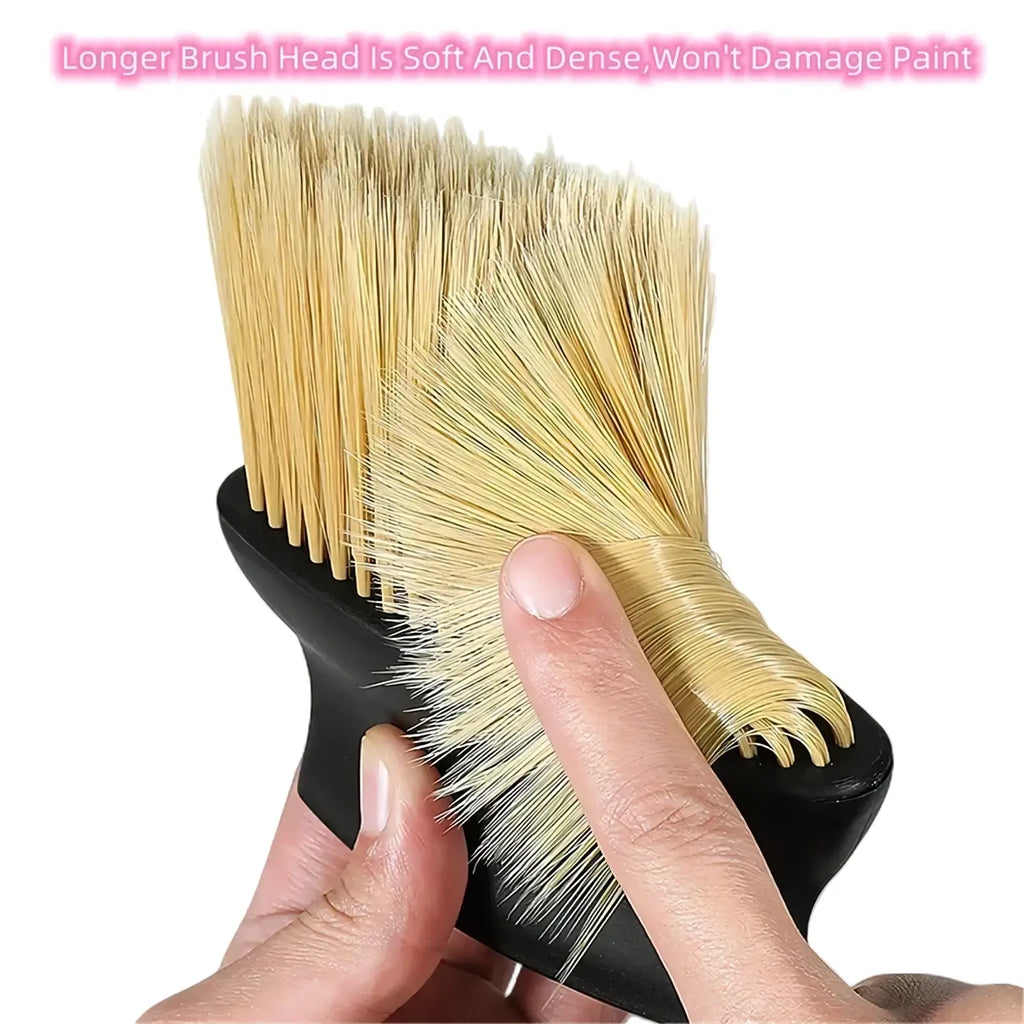 A hand holds a car interior detailing dust brush with black handle and soft dense beige bristles for gentle cleaning