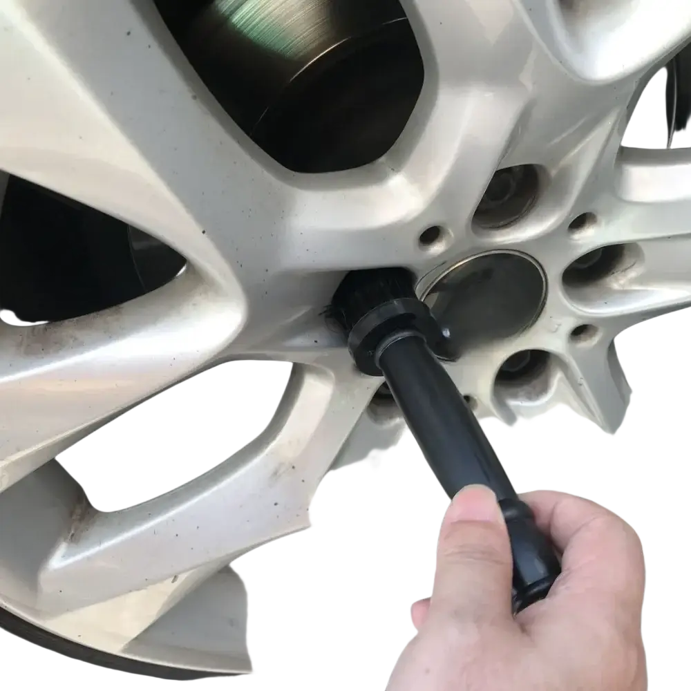 Black lug wrench tightening a bolt on a silver alloy wheel as part of car wheel detailing brush set rim cleaner use