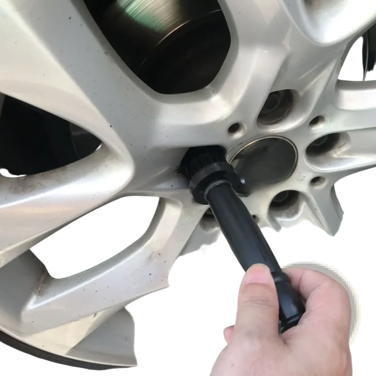 Black lug wrench tightening a bolt on a silver alloy wheel as part of car wheel detailing brush set rim cleaner use
