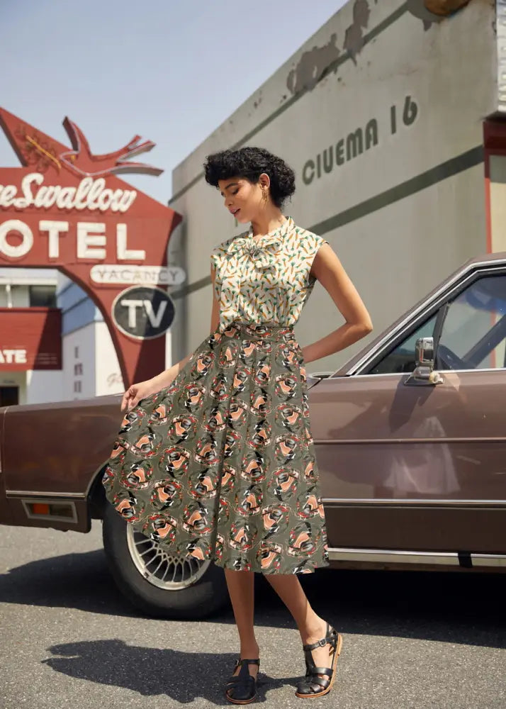 A woman wears a vintage 1950s style sleeveless knee-length dress with a floral carrots print on dark green fabric