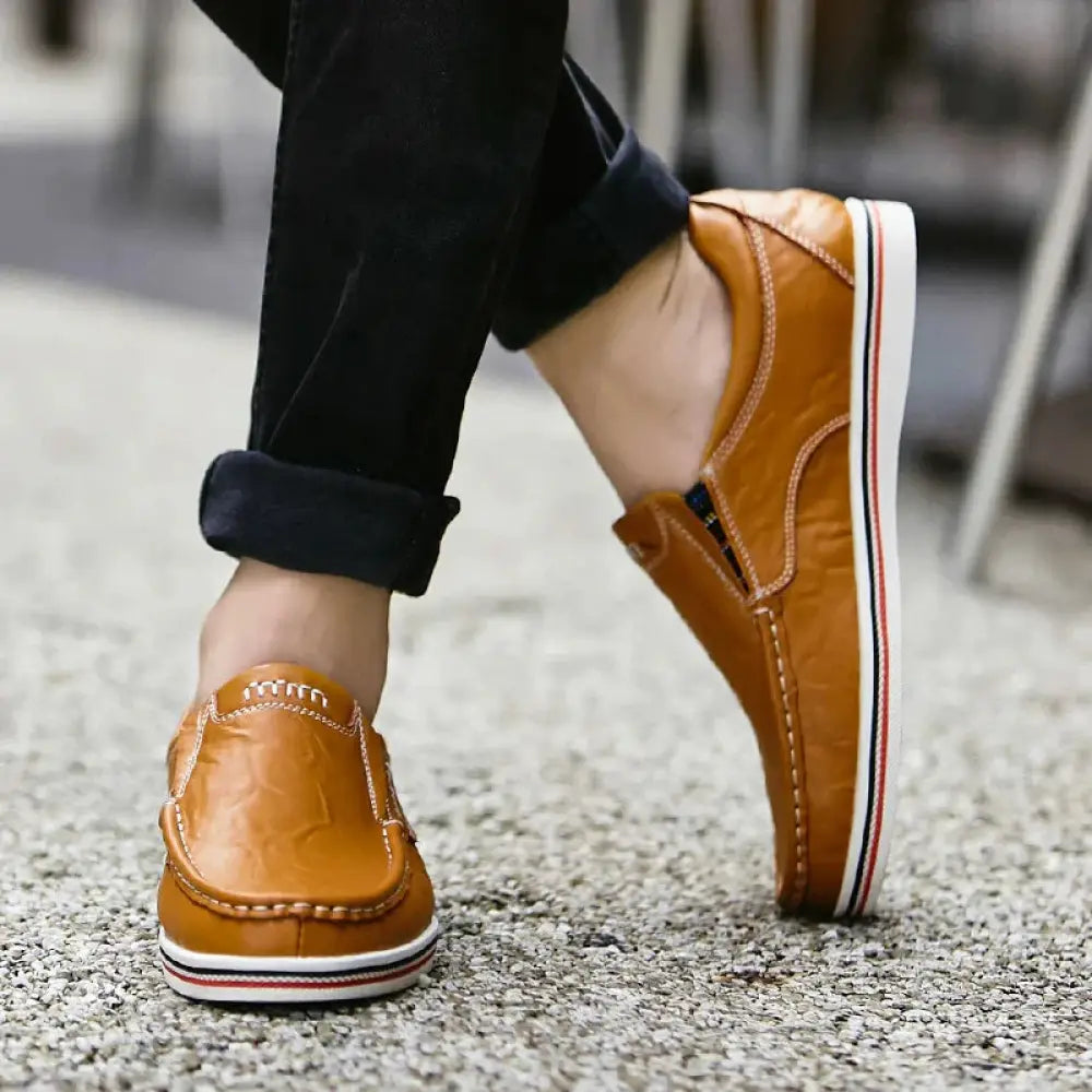 Men’s British leather slip-on shoes in tan with white red and blue striped soles shown from the back side