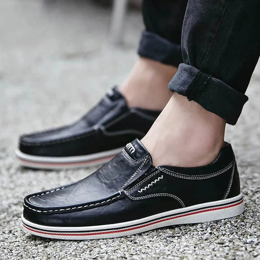 Men’s british leather slip on shoes in black with white stitching and a red and white striped rubber sole