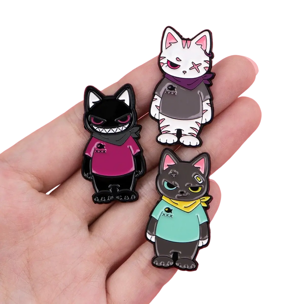 Cat enamel lapel pin set featuring three stylized pins in black, white, and dark gray with distinct colorful accessories