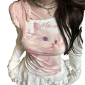 White long-sleeved top with pink cat graphic purple eyes and maxm text layered under sheer lace halter overlay