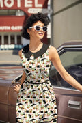 A sleeveless cotton dress with a black peter pan collar featuring black cats and plants on a cream background