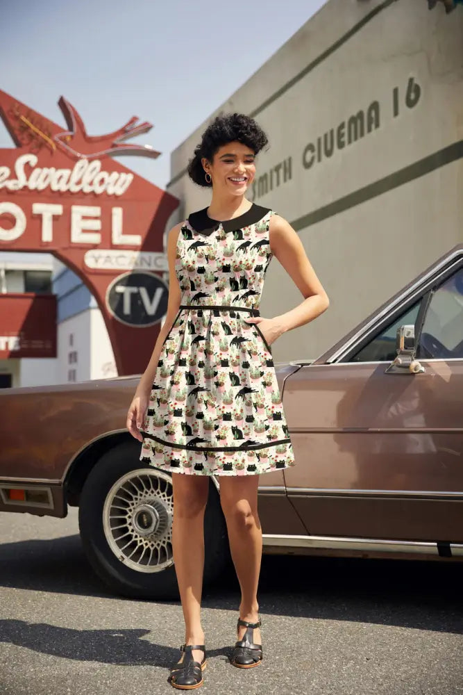 A sleeveless cream cotton dress with black peter pan collar and belt featuring cat print in various poses
