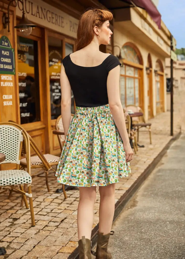 A woman wears a light green cats and plants vintage a-line skater skirt with a colorful cartoon print and a black top