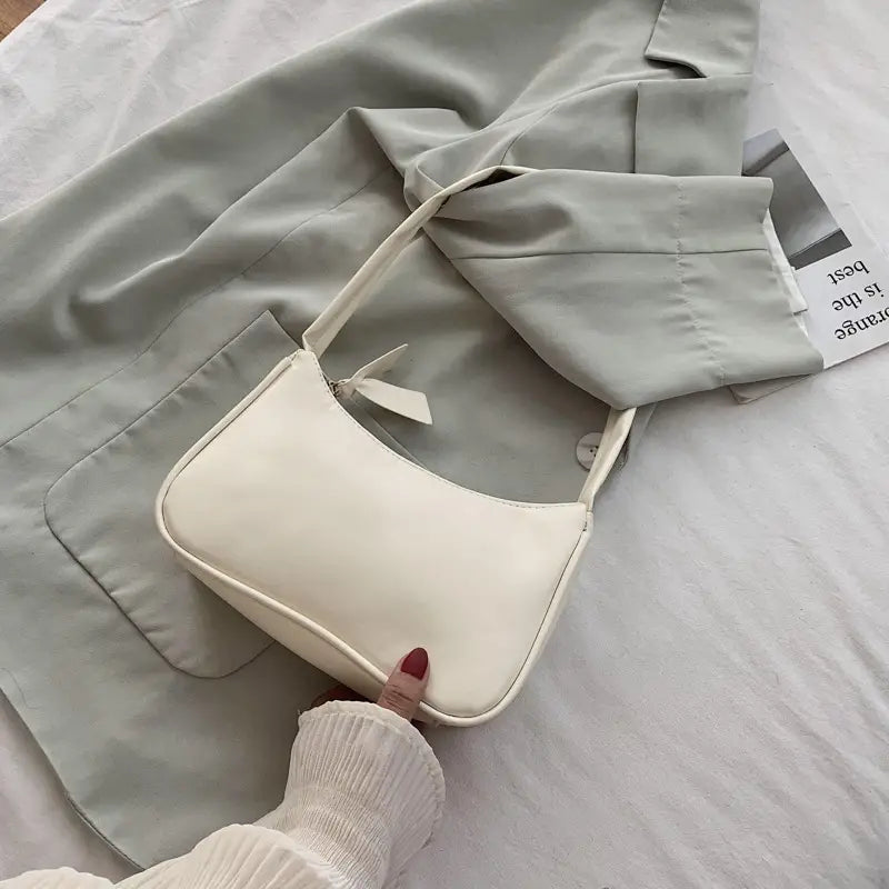 Eine minimalistische Umhängetasche aus Kunstleder mit gebogenem Unterarmgriff in elegantem Off-White, mit minimalistischer Gestaltung und passendem Schulterriemen.