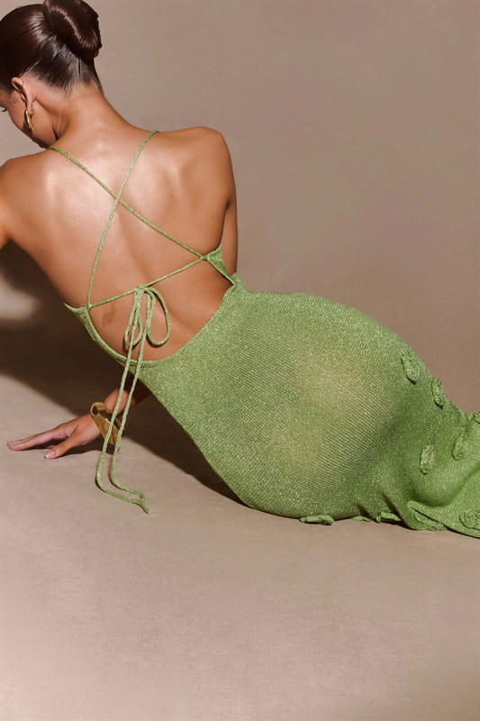 Back view of a shimmering olive green crochet floral lace mermaid maxi dress with glitter accents featuring a knit material, crisscross tie detail, and decorative button-like embellishments along the hem.