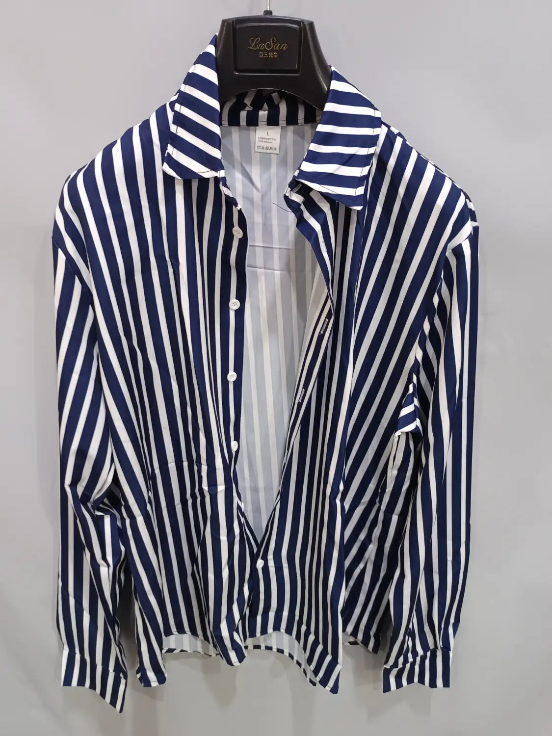 Chemise décontractée à manches longues rayée verticalement bleu marine et blanc pour hommes, avec col classique présenté sur un cintre noir.