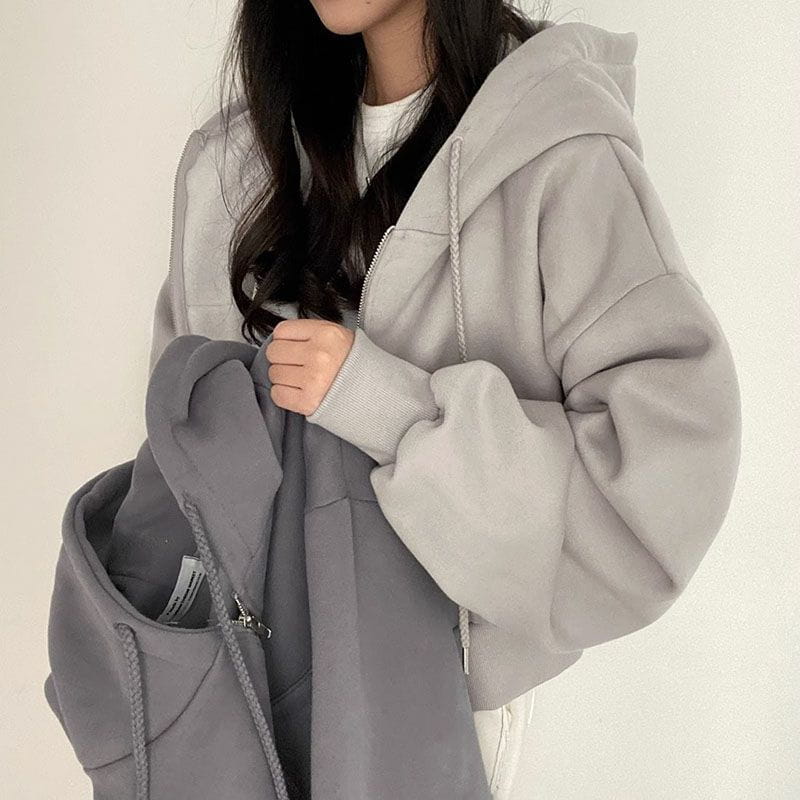 Ein weicher, hellgrauer Zip-up-Kapuzenpullover mit lockerer Passform und dazu passenden Kordeln, gezeigt von vorne, passend zum Produktsortiment eines dunkelblauen Samt-Velours, wattierten Kapuzenpullovers mit schmaler Passform.