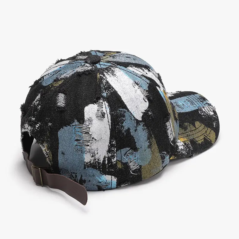 Une casquette de baseball en coton à projections de peinture vieillies, présentant un design abstrait audacieux dans des tons noir, blanc, bleu et or.