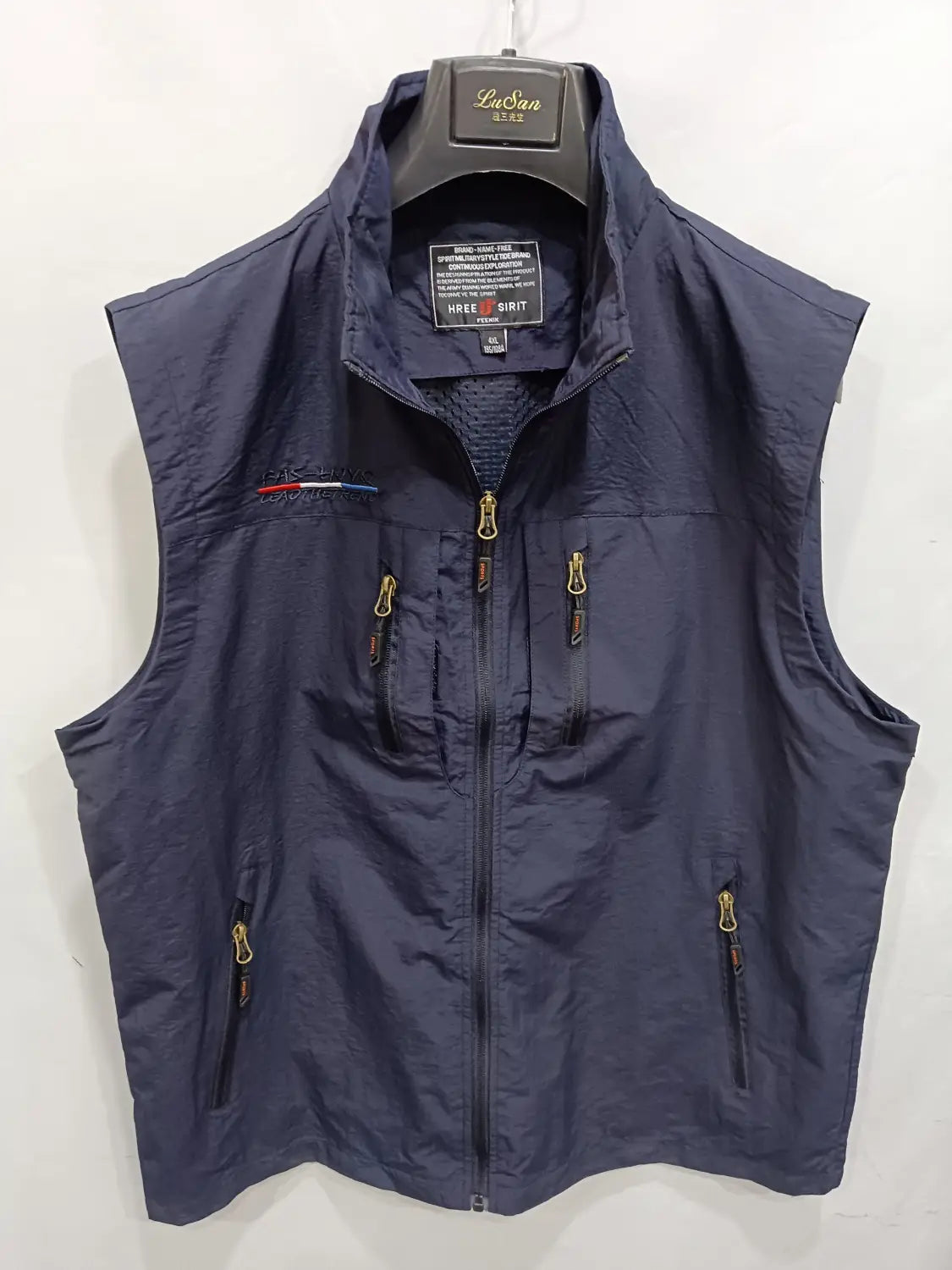 Chaleco utilitario sin mangas para hombre en azul marino oscuro con varios bolsillos, cremalleras con acabado dorado y un pequeño logotipo bordado en el lado izquierdo del pecho.