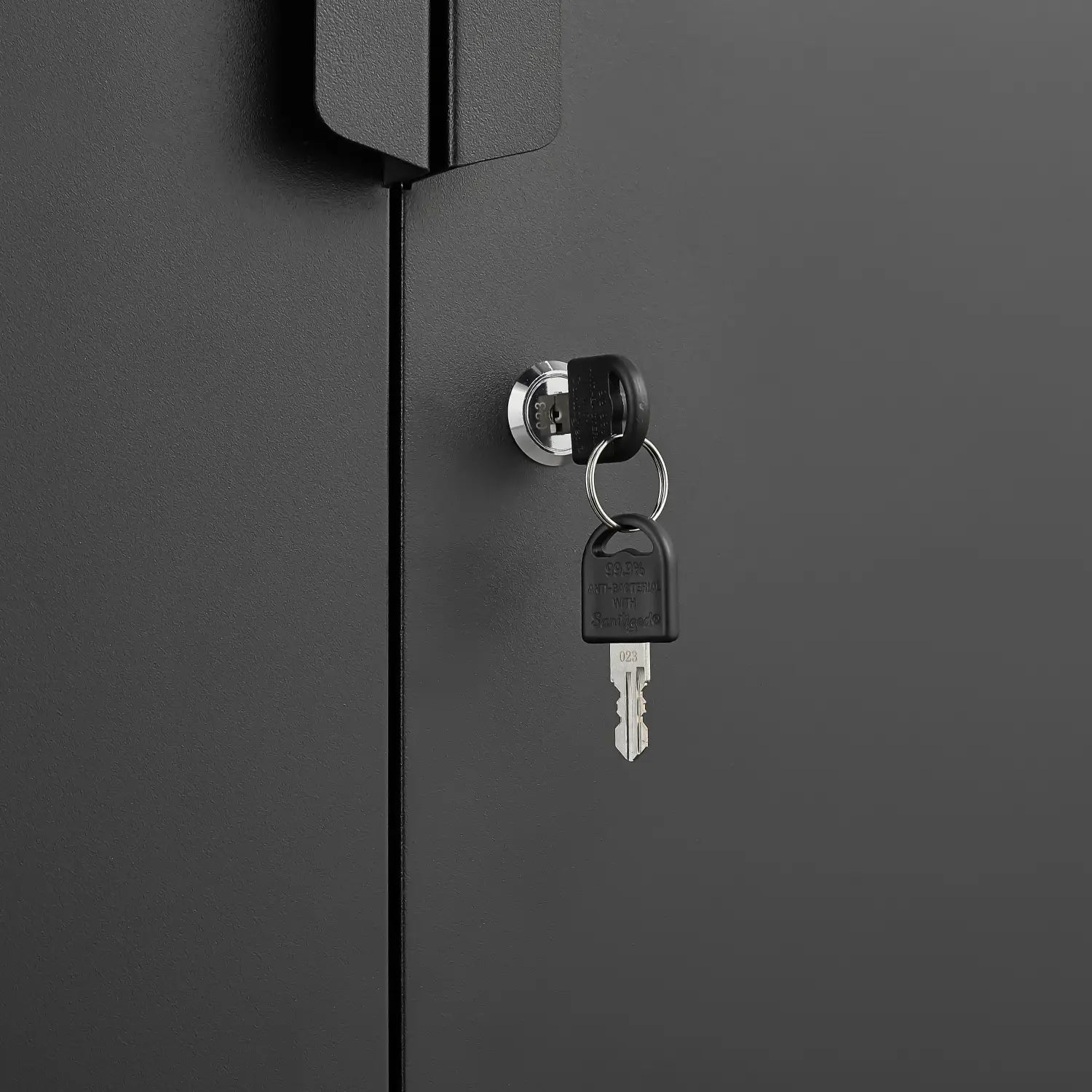 black key with plastic head and metal blade inserted into circular chrome lock on dark gray steel locking file cabinet door with four shelves