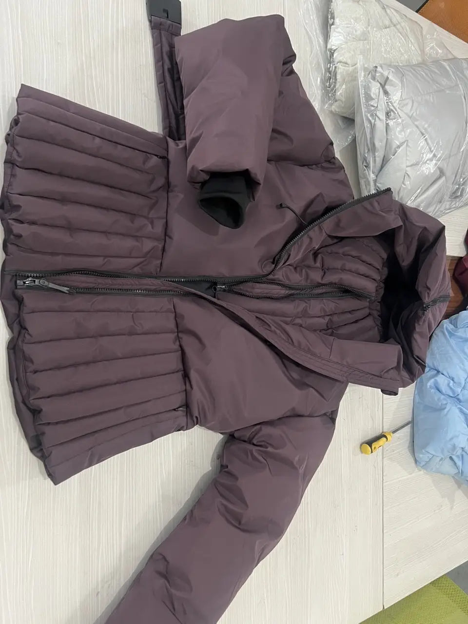 Women’s belted hooded puffer coat in deep plum quilted fabric with black zipper accents and ribbed cuffs.