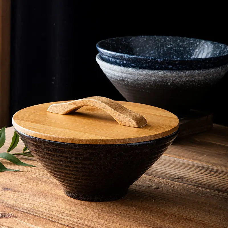Dunkelkeramische Japanischschale mit einer strukturierten, gerippten Oberfläche und einem hellen Holzdeckel mit gebogenem Griff aus dem Set „rustikale gesprenkelte Tischgeschirre“.