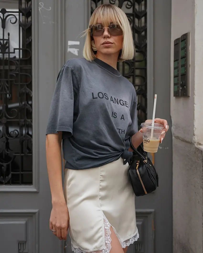 グレーのオーバーサイズTシャツに「ロサンゼルス」を黒文字でプリントし、サテンレースのAラインミニスカートと組み合わせたコーディネート。