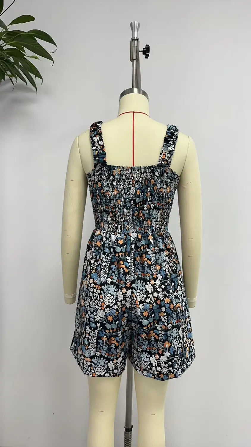 Mono fruncido de estampado floral azul oscuro con tirantes finos y cintura ajustada, presentado en un maniquí diseñado como un mono-jumpsuit de playa de verano sin mangas.