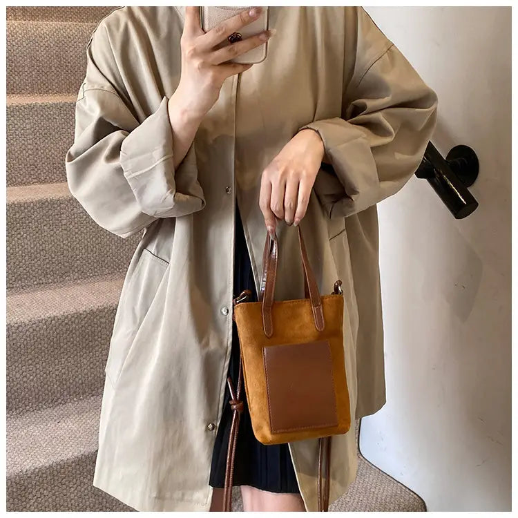 Tan suede mini bucket crossbody bag with retro leopard print, featuring a contrasting brown leather front panel and handles.