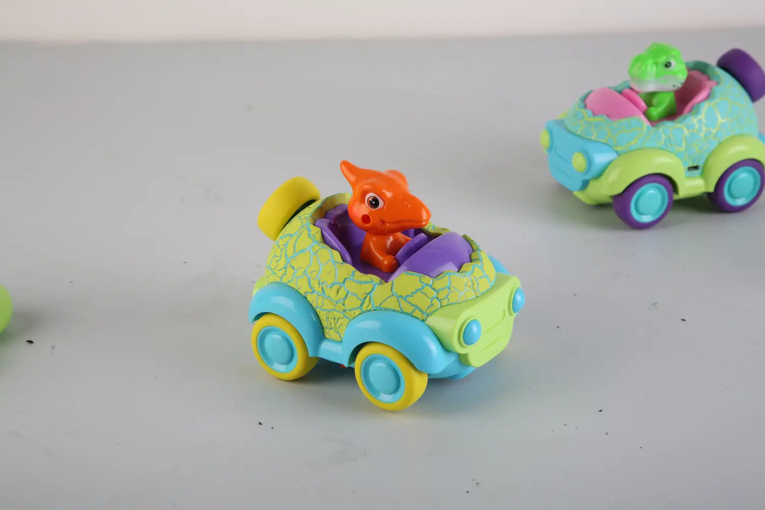 A vibrant green and blue plastic dinosaur remote control car for toddlers with a yellow textured roof and an orange dinosaur driver inside.