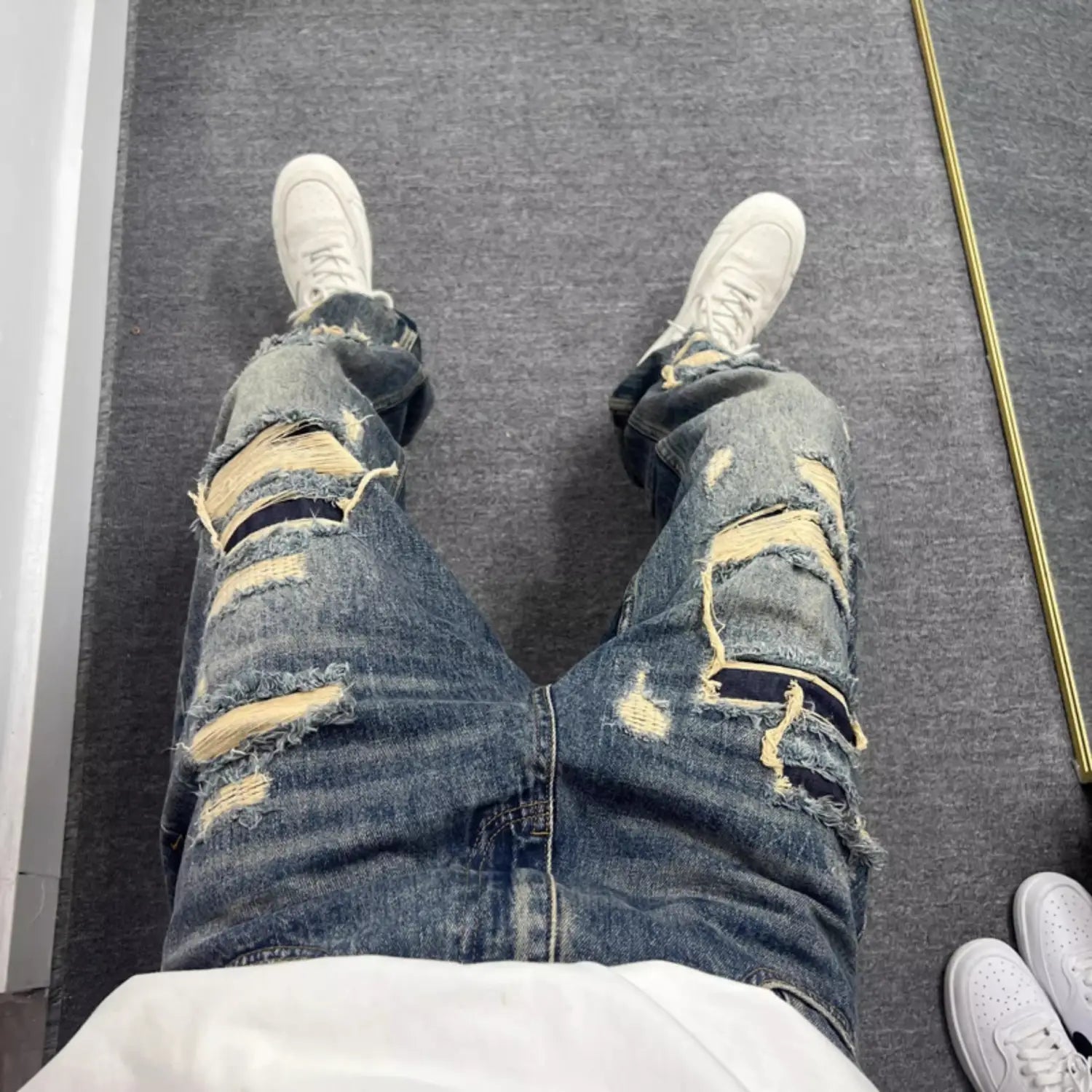 Men’s light blue distressed ripped patch denim jeans made of blue denim with prominent ripped and frayed patches on the thighs