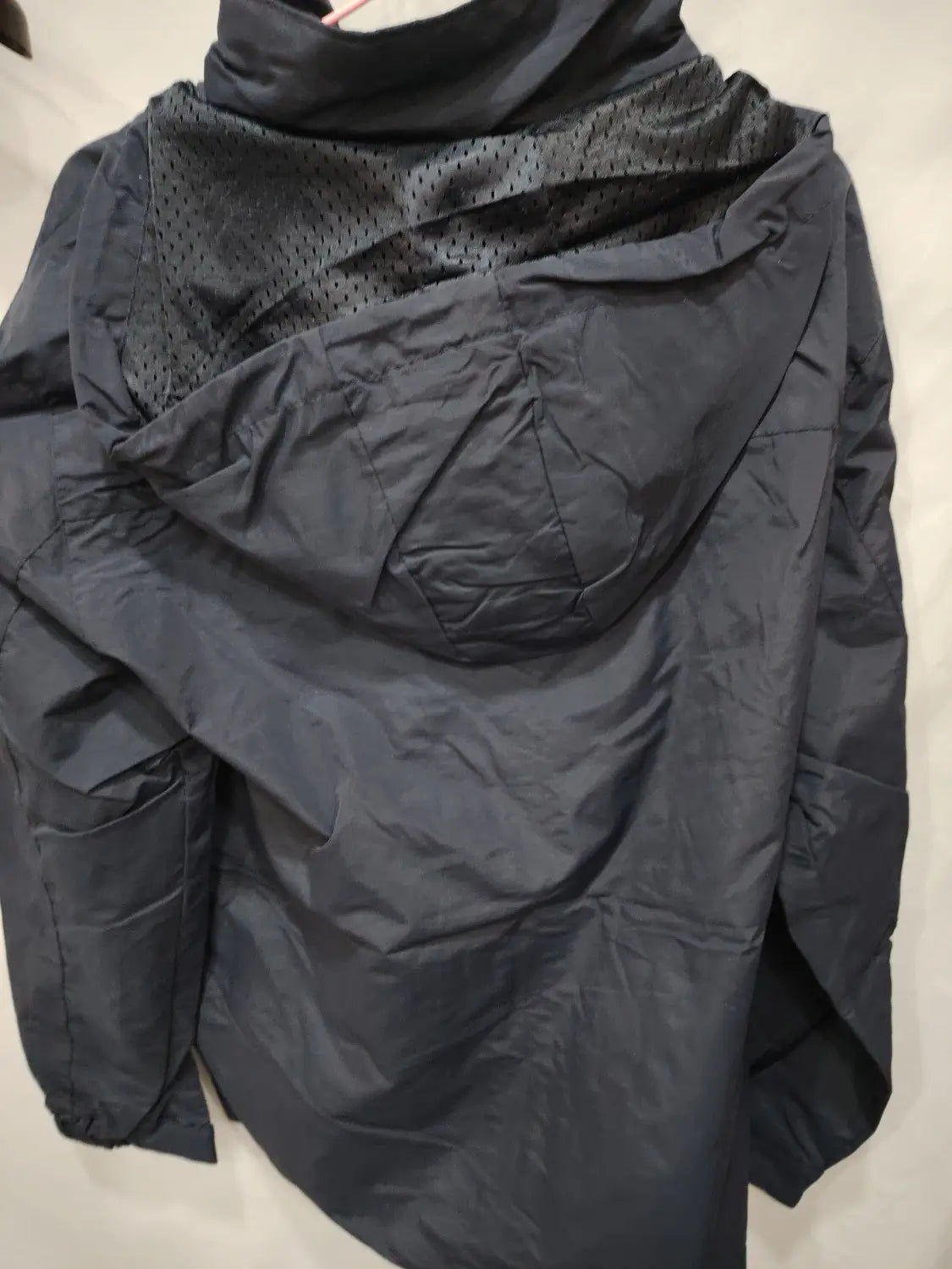 Chaqueta de senderismo con capucha impermeable color negro, con panel de malla en el cuello y tejido ligero ligeramente brillante mostrado desde el lado posterior