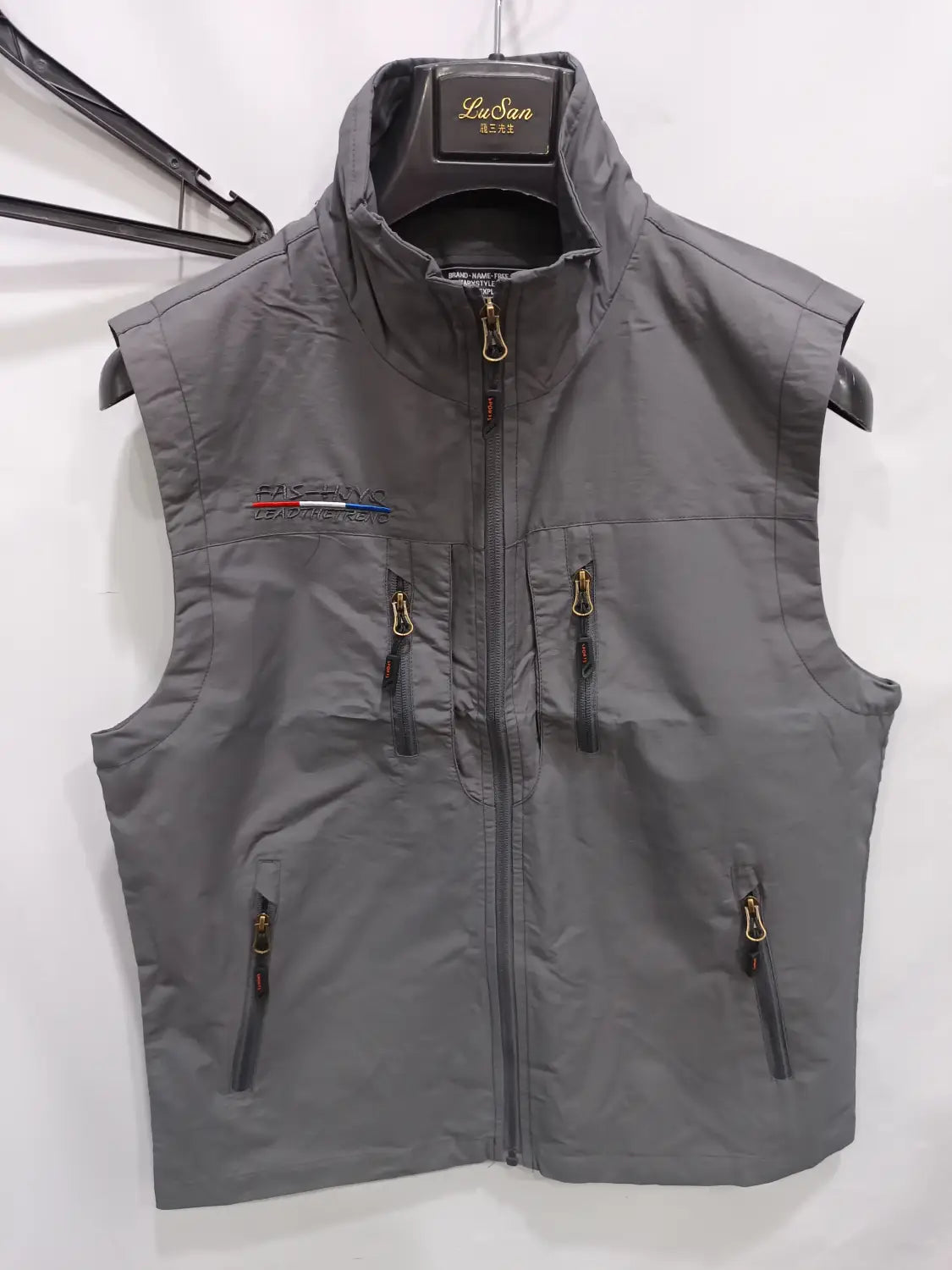 Chaleco utilitario con capucha y múltiples bolsillos para hombre sin mangas de la marca Lusan en color gris, con cuello alto, cierre con cremallera frontal y varios bolsillos con cremallera.