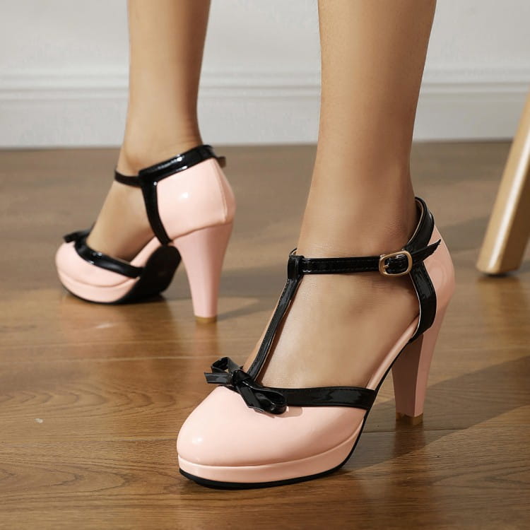 Pink patent leather platform high heels with black t-strap and bow at the toe.