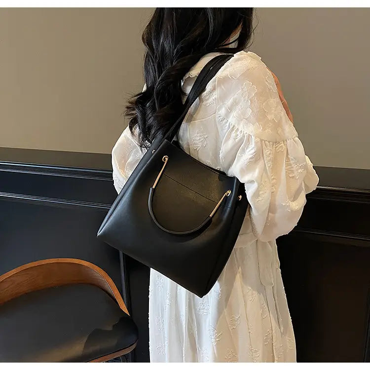 Black leather minimalist bucket bag with gold-tone metal handles hardware and detachable strap.