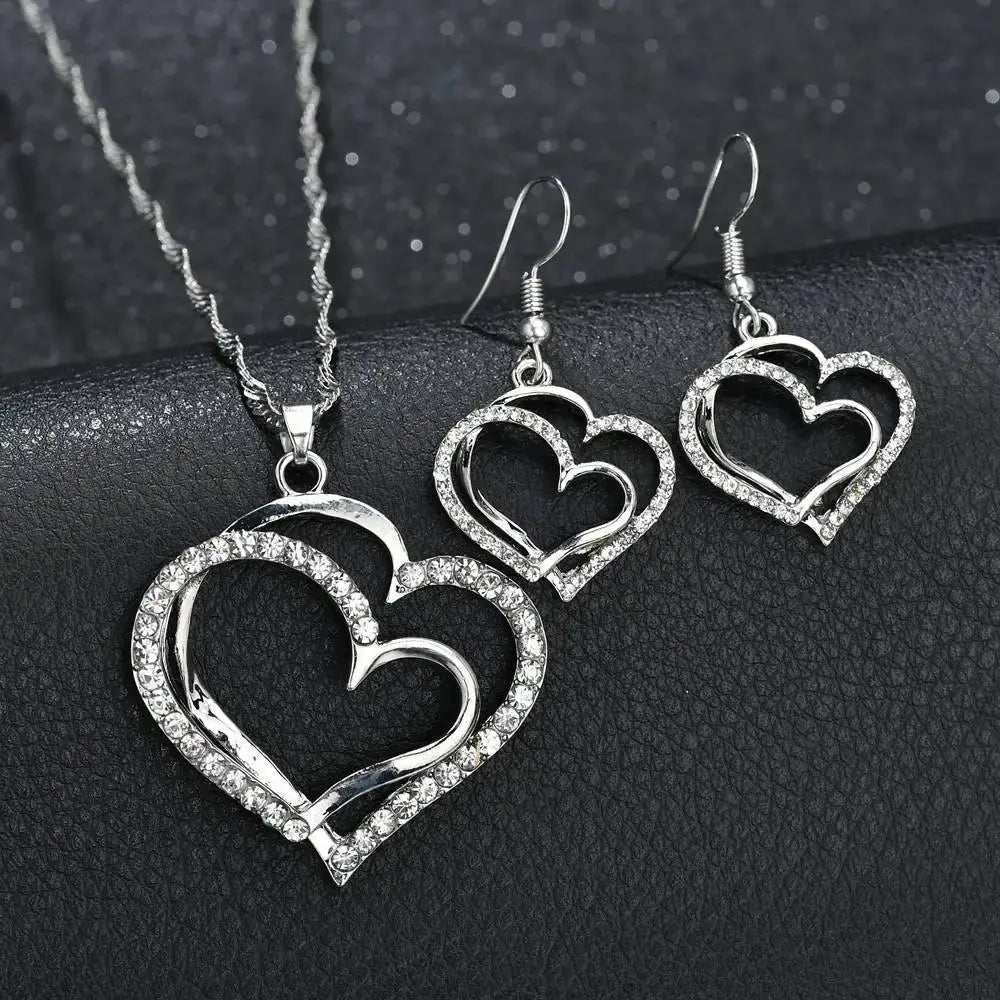 Elegant rhinestone heart jewelry set featuring a silver heart-shaped pendant necklace and matching earrings with intricate overlapping designs adorned with sparkling rhinestones.