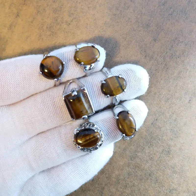 A collection of five natural gemstone tiger eye rings featuring polished amber brown stones set in silver tone metal with oval and rectangular cuts.