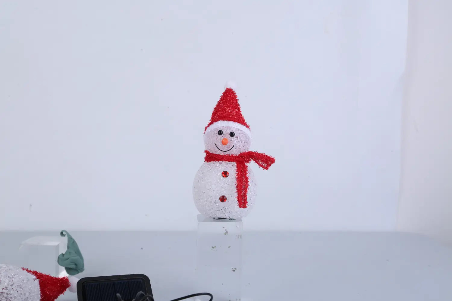 Un brise-soleil d’extérieur de jardin en forme de bonhomme de neige solaire blanc festif, avec un bonnet et une écharpe rouges scintillants et trois boutons rouges, conçu pour une décoration extérieure étanche.