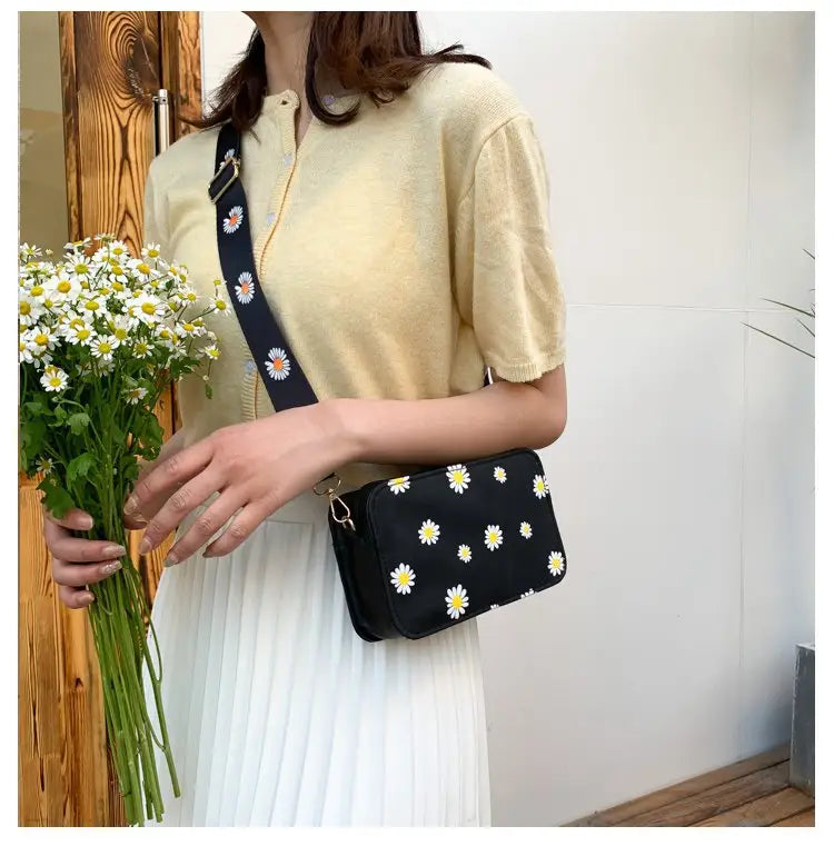 Black crossbody bag made of pu leather with white daisy embroidery and a matching navy chain strap featuring the same floral pattern.
