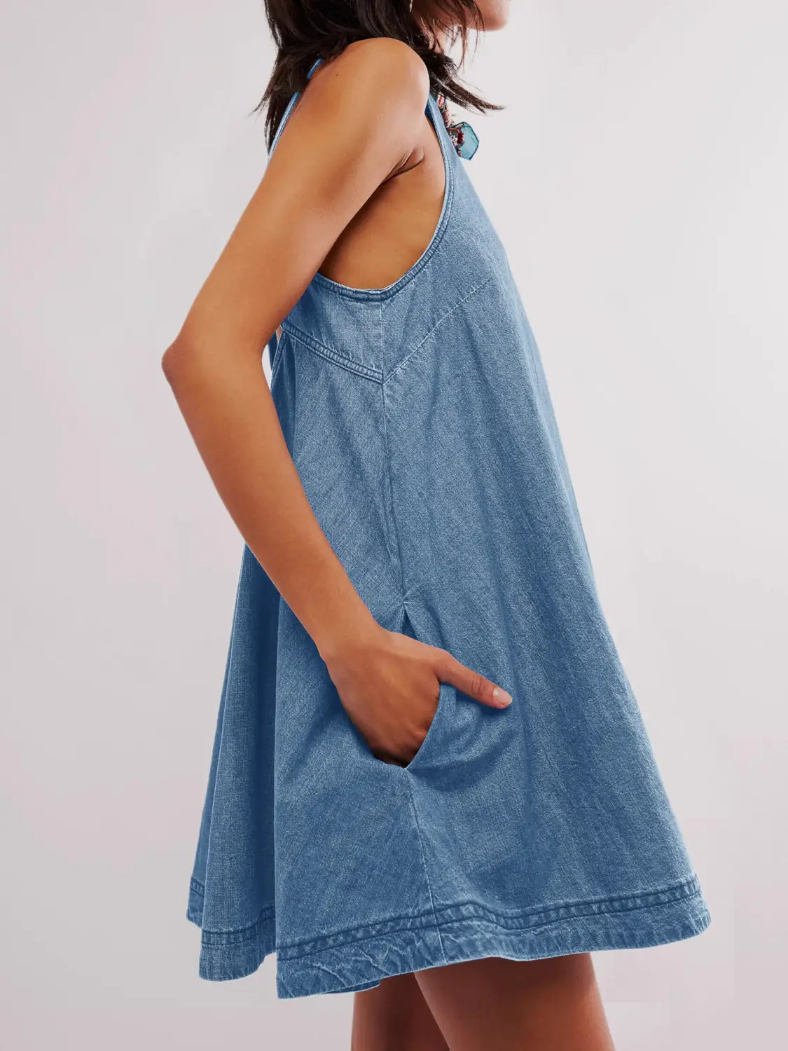 Ein hellblaues Jeans-Minikleid mit entspannter Passform, ärmellosem Design, Fronttaschen und einem hinten offenen Schleifen-Detail.