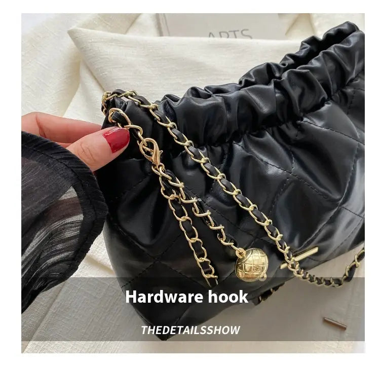 Black quilted faux leather crossbody bag with gold-tone chain strap and globe-shaped charm.