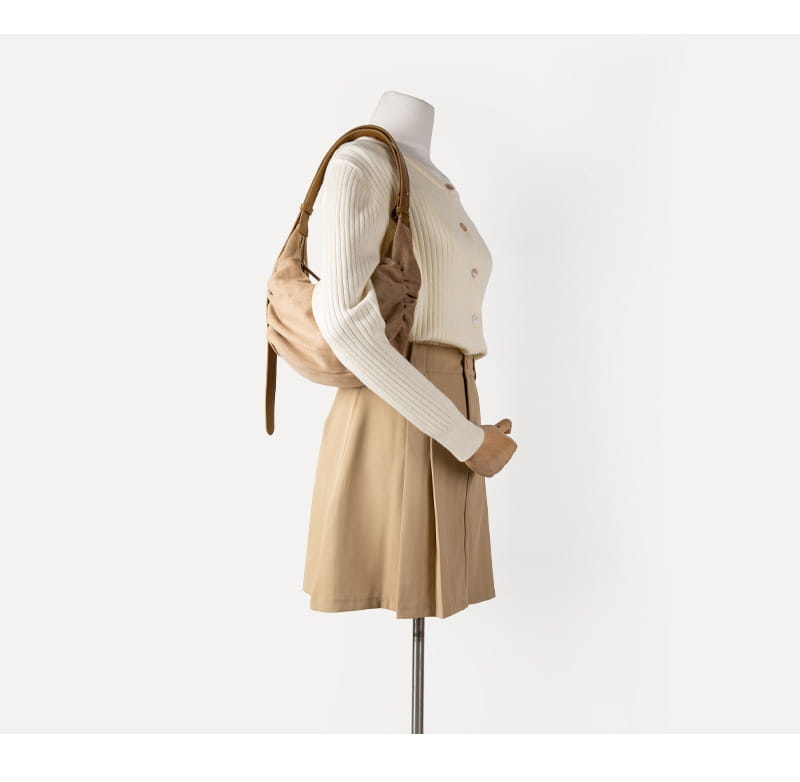 Beige leather suede dumpling shoulder bag with brown straps worn over a mannequin designed as a slouchy crossbody hobo.