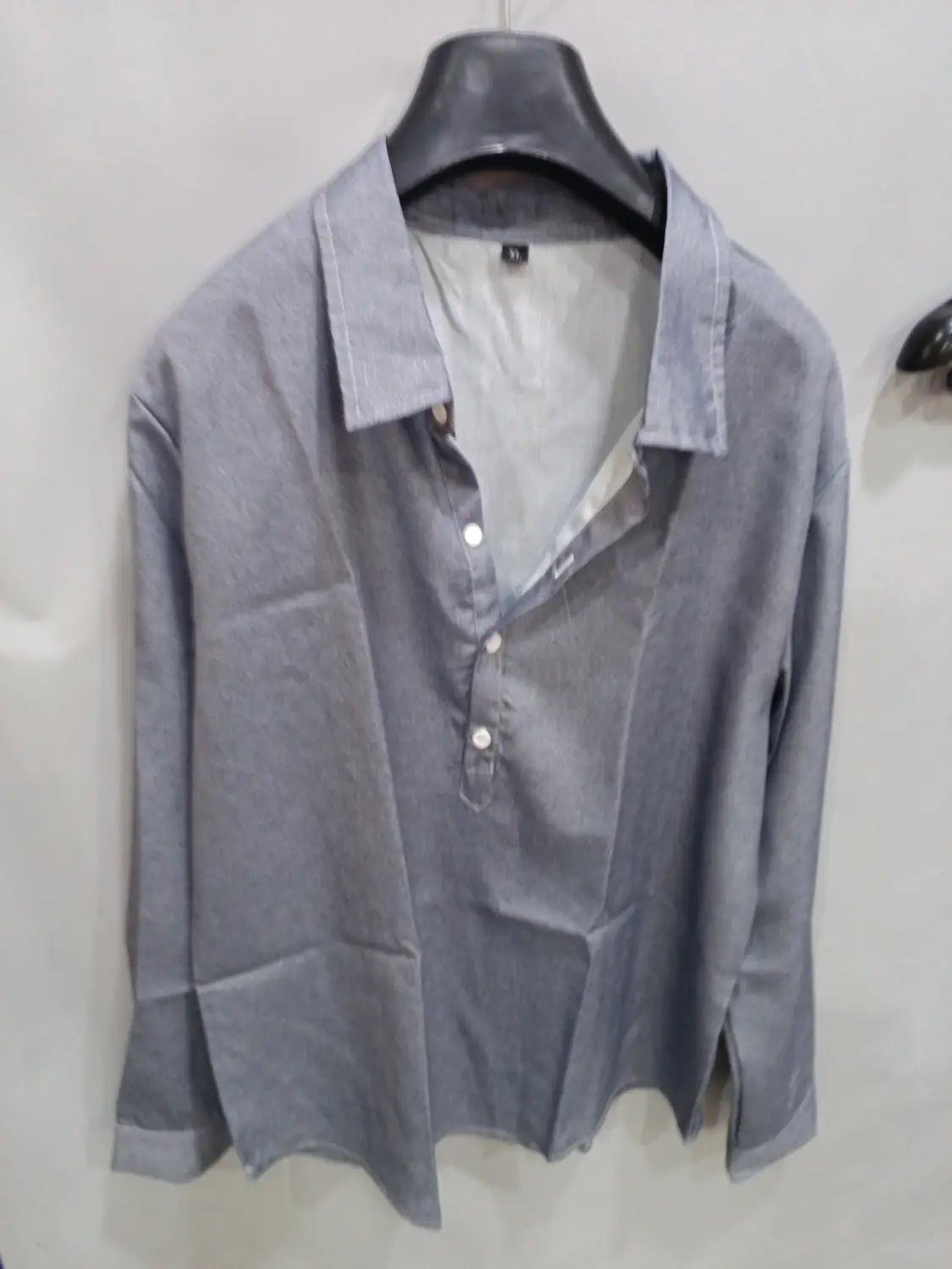 Herren-Jeanshemd-ähnliches, strukturiertes Hemd mit langen Ärmeln, grau, mit Kragen und weißen Knöpfen, die an einem schwarzen Bügel hängen.
