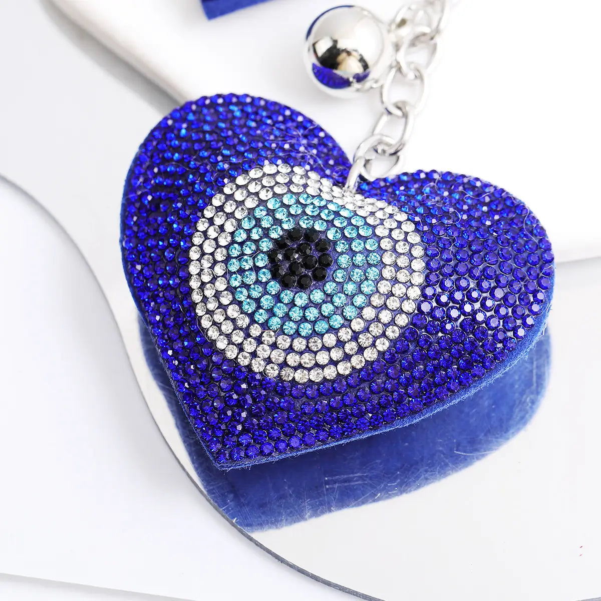 Blue heart-shaped leather keychain adorned with blue rhinestone evil eye design featuring a silver bell and chain.