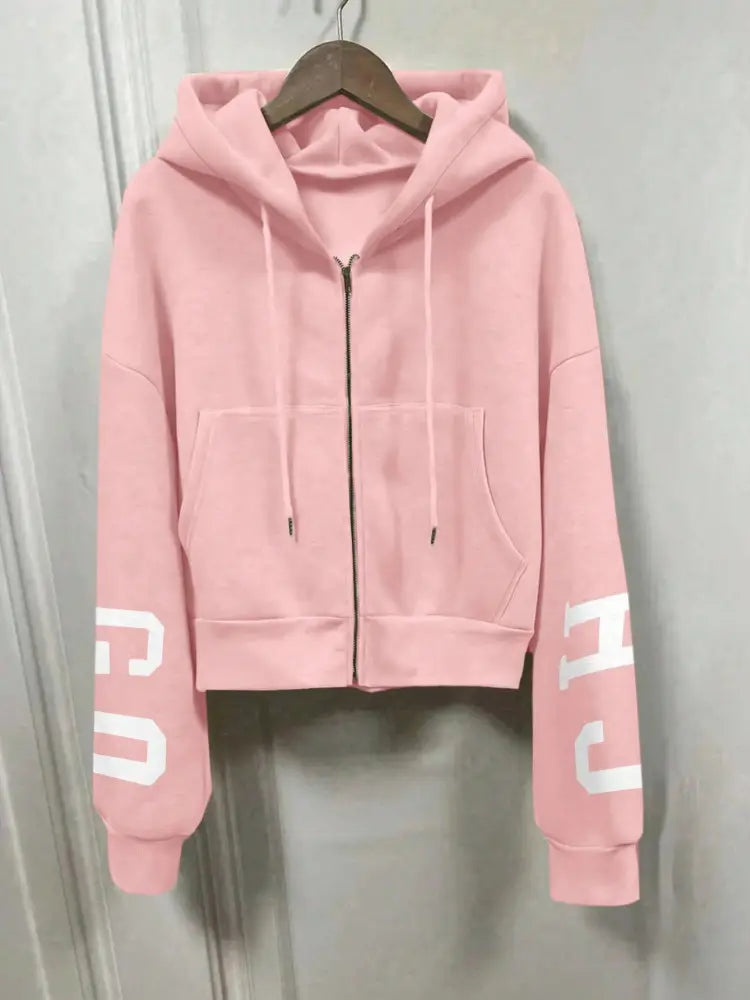 Sweat-shirt à capuche zippé imprimé graphique rose court, avec des lettres blanches sur les manches, une fermeture éclair à l’avant et des cordons.