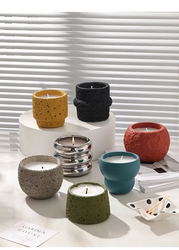 Une collection de supports de bougie en ciment à effet moucheté, colorés, en jaune, noir, rouge, sarcelle, vert et argent, conçus comme des coupelles d’aromathérapie.