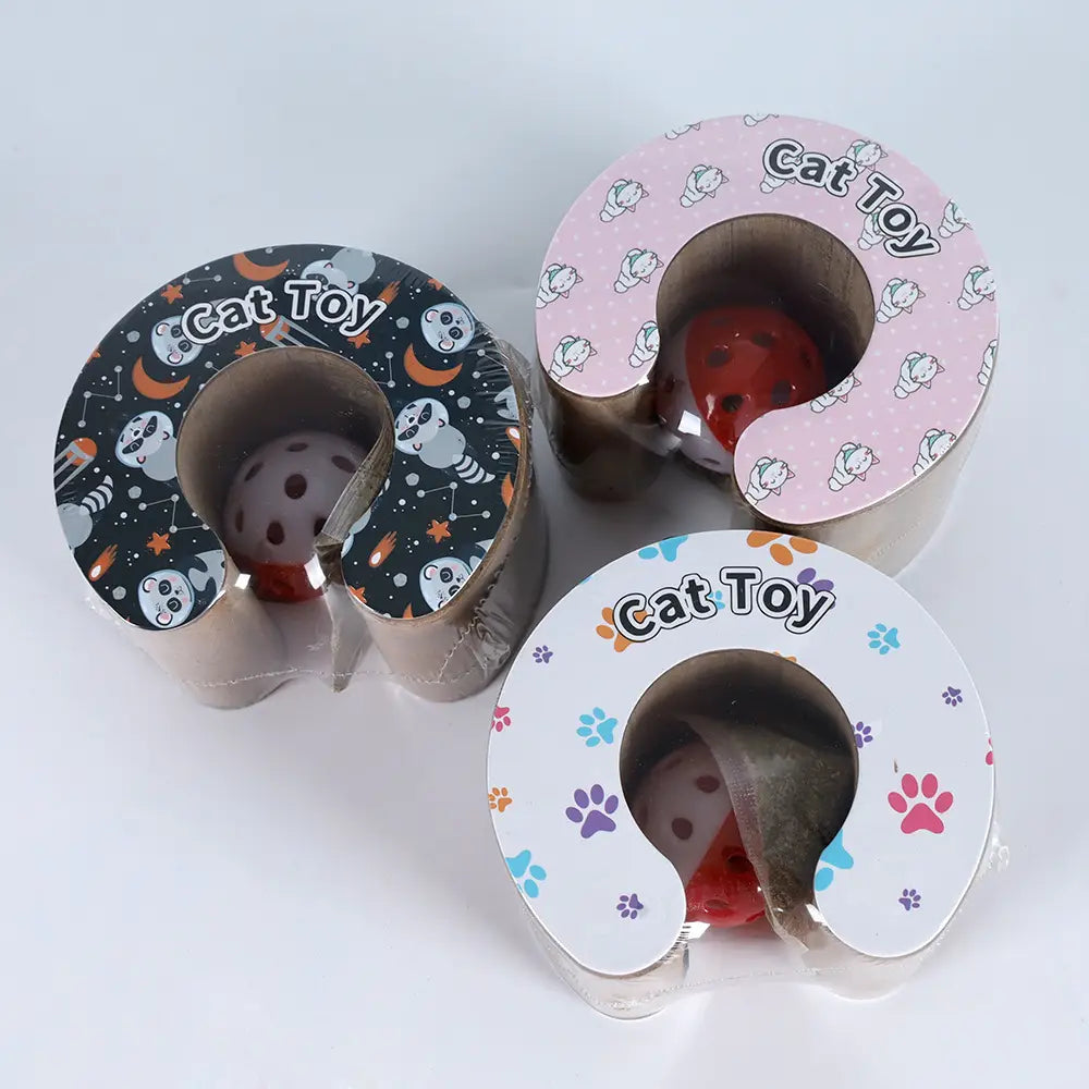 Tres juguetes plegables magnéticos con tablero rascador circular para gatos de cartón, envueltos en un embalaje impreso de colores con diseños de caricaturas e interiores con forma de bolas rojas y grises.