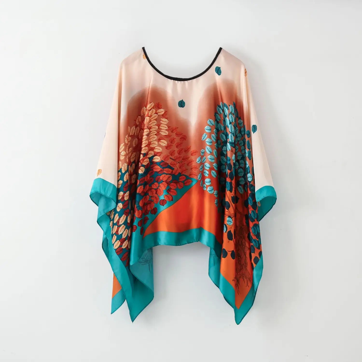 Printed silk patterned pullover shawl cape in peach tone with vibrant autumnal orange and teal leaf print and black trim on neckline and cuffs.