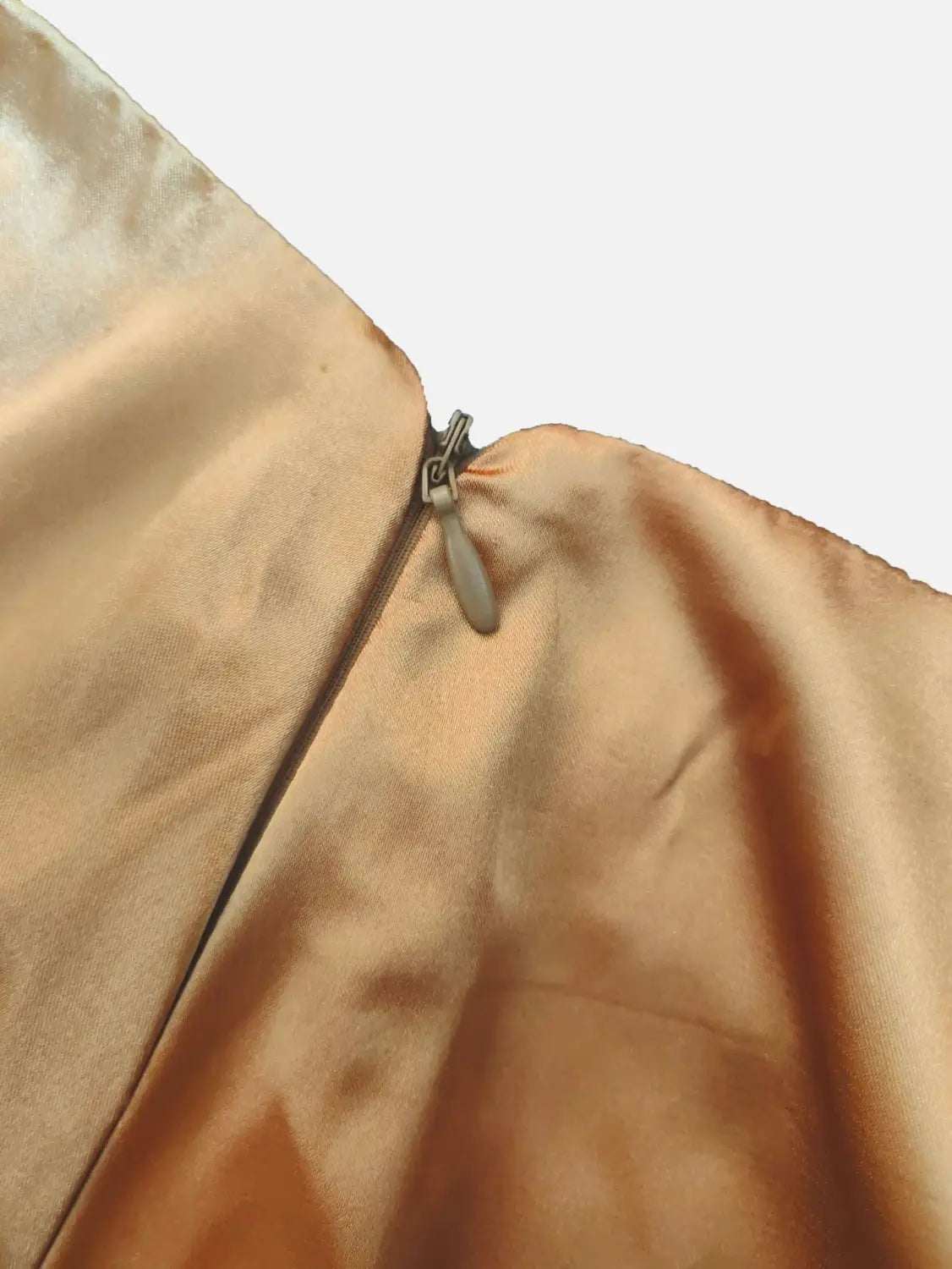 eine Nahaufnahme eines beigen Satin-Reißverschluss-Zippers auf einem roségoldenen Satinkleidrock (Midi) aus Seidenstoff mit hoch sitzendem, fließendem Fall