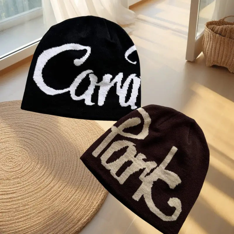 black and dark brown knit beanie hats featuring bold white cursive embroidered lettering on a soft knit material