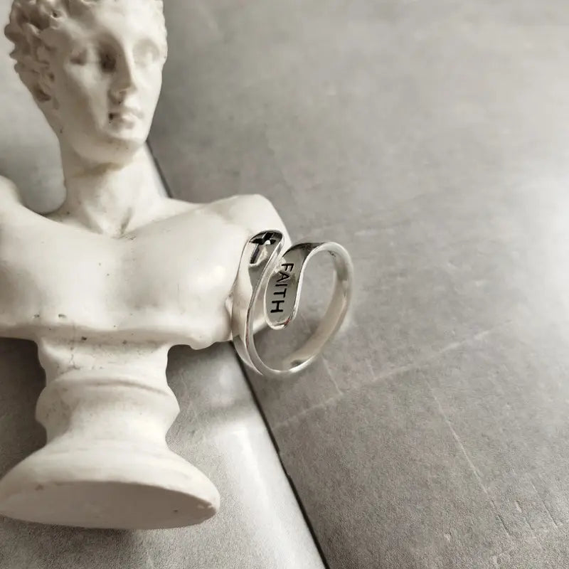 A sleek silver faith cross wrap ring with an adjustable band featuring a modern open design and faith engraved on its inner surface.