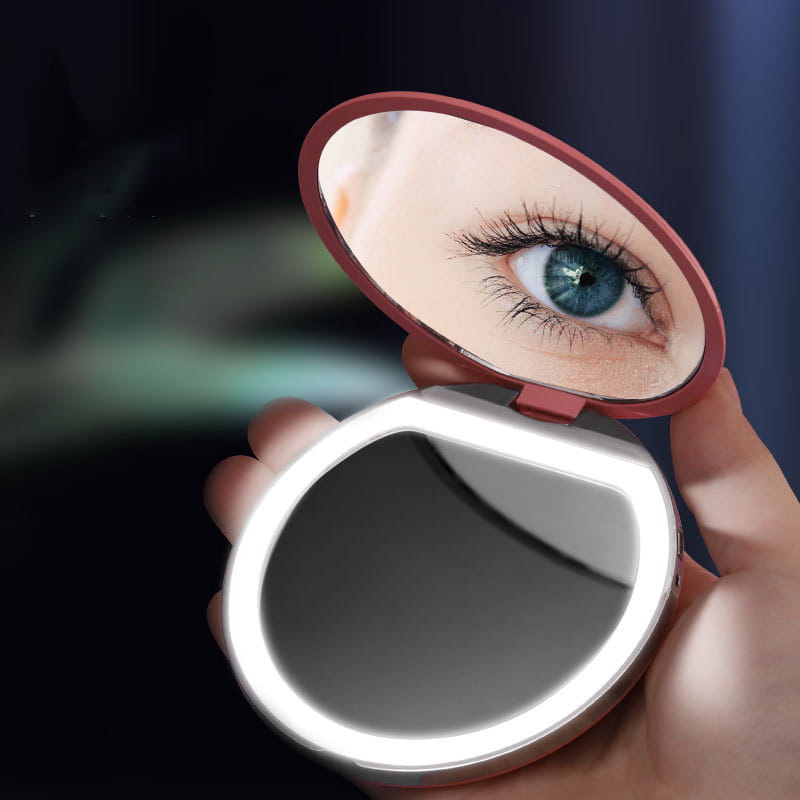 Un espejo de maquillaje LED compacto con forma ovalada y marco en color rosa dorado, con un anillo iluminado, diseñado para el uso USB portátil y la comodidad del plegado.