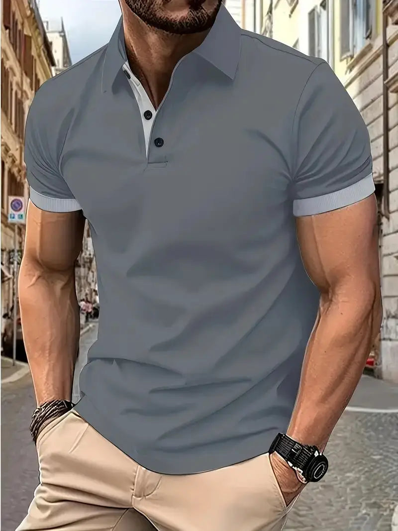 Ein graues Herren-Poloshirt mit kurzem Ärmel, kontrastierendem weißem Innenkragen und Ärmelmanschetten sowie schwarzen Knöpfen, entworfen für den Freizeitgebrauch.