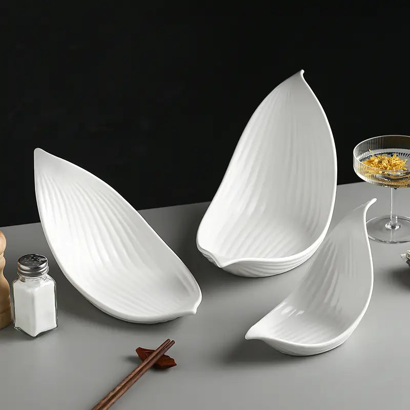 Three white ceramic plates shaped like leaves with subtle vertical ridges designed as irregular serving dishes.