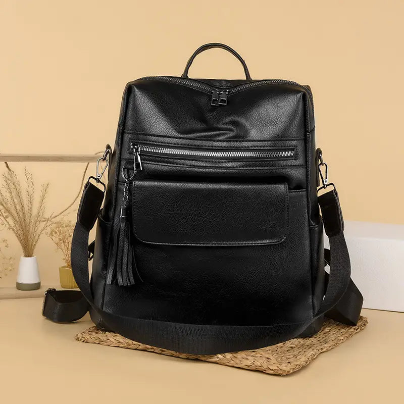 Black faux leather one shoulder backpack 35cm featuring multiple zippers and tassel detail.